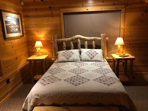 A cozy wooden cabin room with a large bed, two bedside lamps, and a framed picture on the wall. - The Snow Goose Lodge (Jamestown)