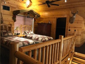 A cozy log cabin bedroom with a bed, a wooden headboard, a ceiling fan, and a mounted deer head. - The Snow Goose Lodge (Jamestown)