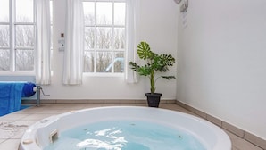 Een bubbelbad in een kamer met een groot raam, een potplant en een blauwe handdoek op de vloer.