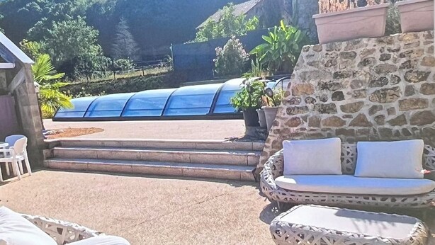 Un patio con mobiliario de mimbre, un muro de piedra y vistas a una piscina azul.