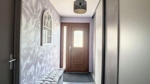 Un pasillo con un banco, una lámpara de techo con diseño y una puerta con ventana.