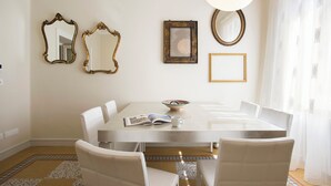 A dining area with a white table, four chairs, and a chandelier. There are three mirrors and two framed pictures on the wall. - Elegant, New, Spacious 3Bedroom Home Between Vatican, Piazza Navona & Trastevere (Roma)