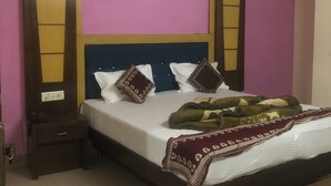 A bedroom with a bed, pillows, a bedside table, and a power outlet. - Hotel Darpan Palace (New Delhi)