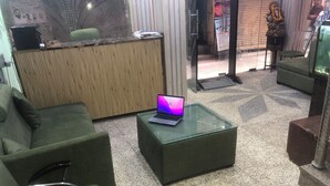 A reception area with a green sofa, a glass coffee table with a laptop, a wooden reception desk, and a patterned floor. - Hotel Darpan Palace (New Delhi)