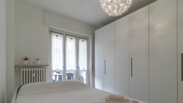A modern bedroom with a large bed, white wardrobe, and a view of the outside. - Turati Family Apartment | Balcone e posto auto (Lecco)