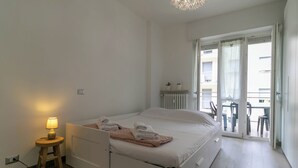 A modern bedroom with a bed, bedside lamp, and a view of the balcony. - Turati Family Apartment | Balcone e posto auto (Lecco)