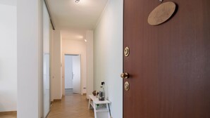 A hallway with a wooden floor, a white door with a brass handle, and a small table with a bottle and a basket. - Turati Family Apartment | Balcone e posto auto (Lecco)