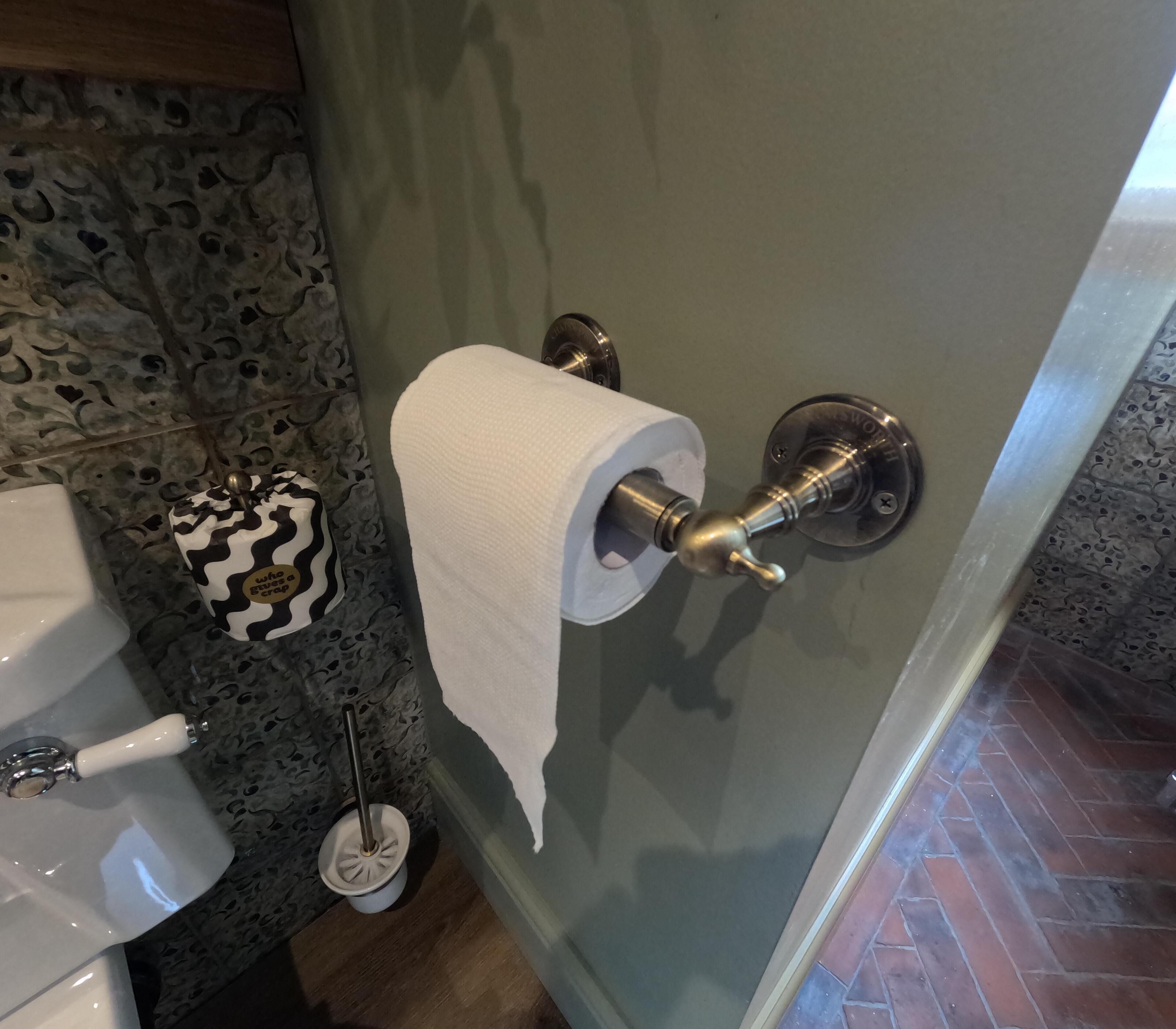 A bathroom with a toilet, a toilet paper holder, a hand dryer, and a patterned trash can.