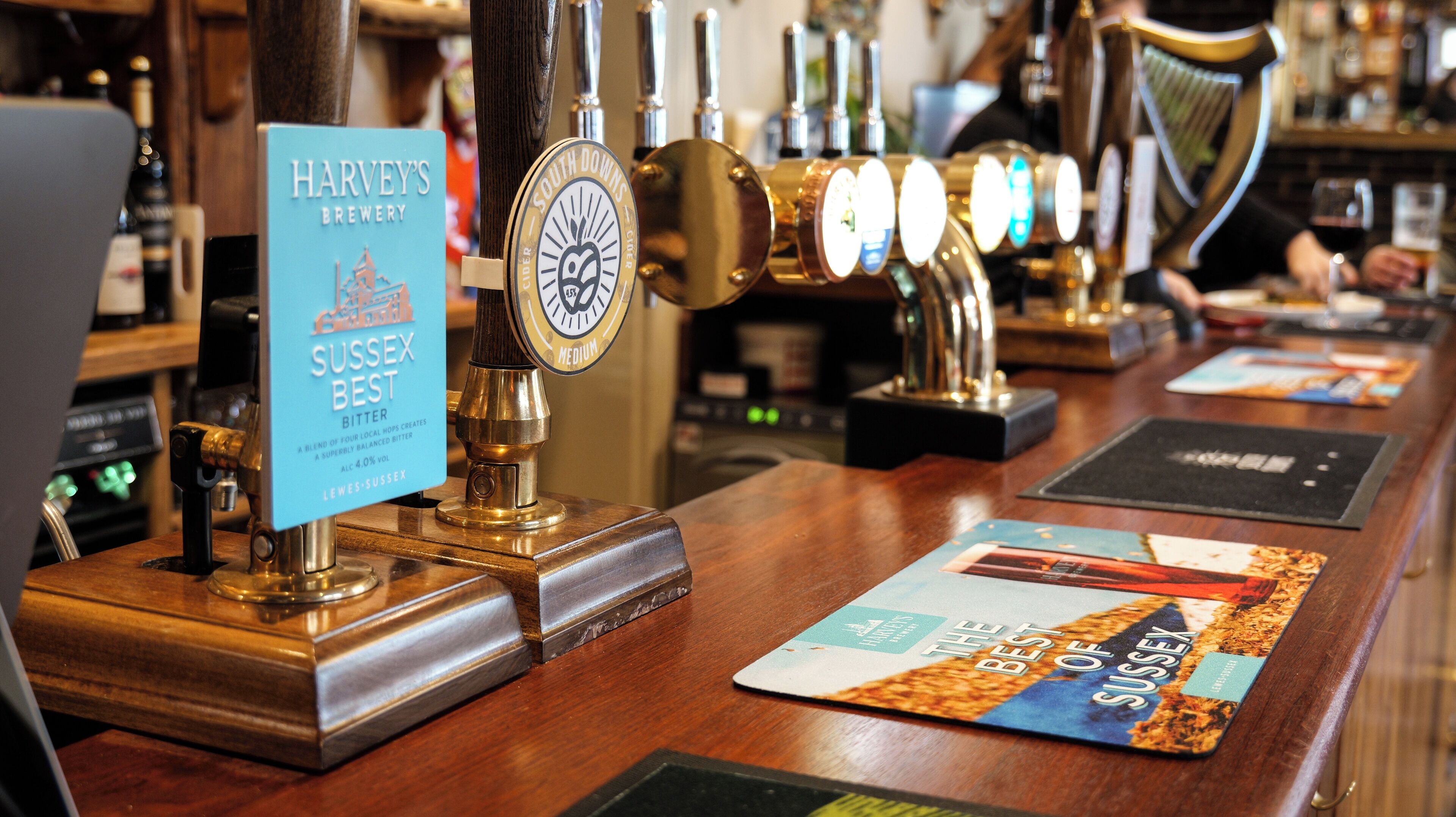 A bar with multiple beer taps, a sign for 'Harvey's Brewery Sussex Best Bitter', and a menu board.