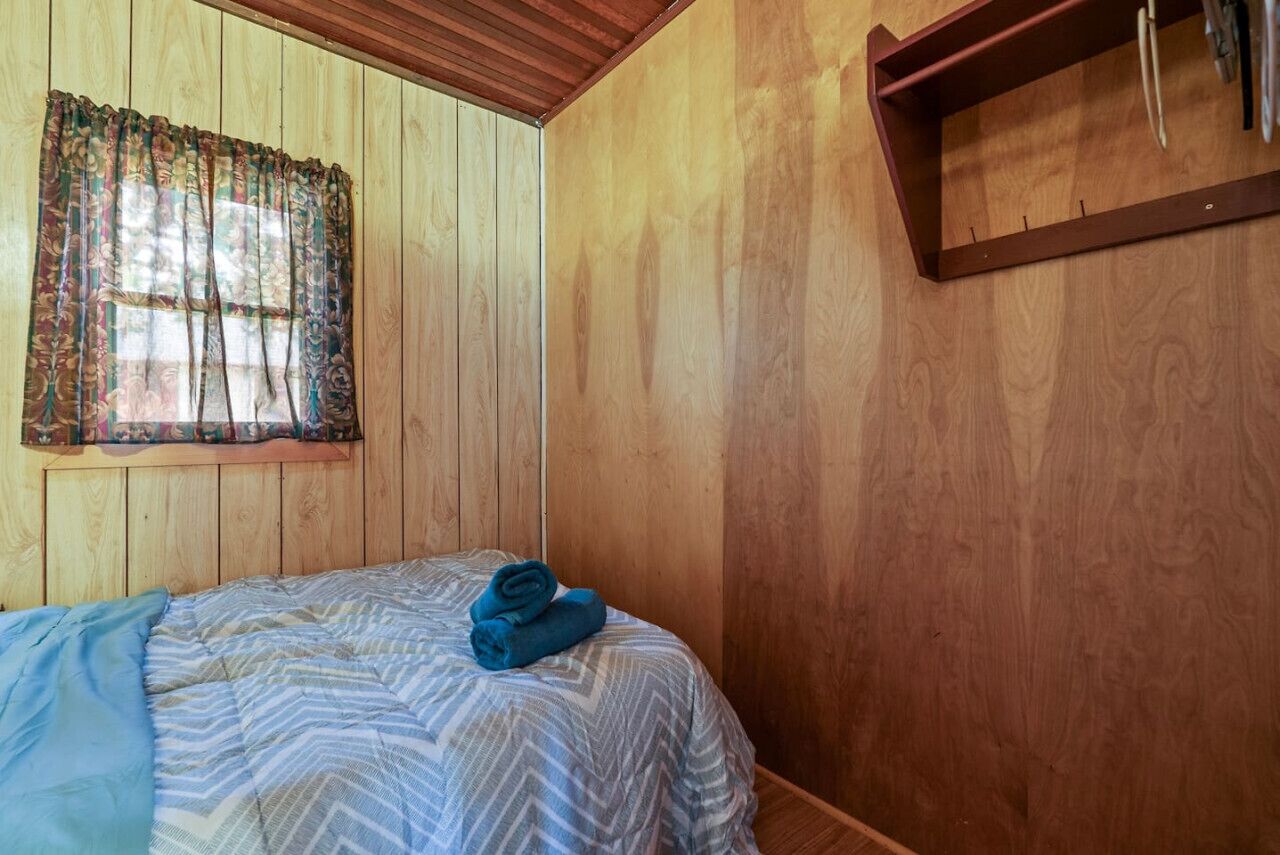 Una habitación con paneles de madera, una cama, un ventanal con cortinas y una estantería de madera.