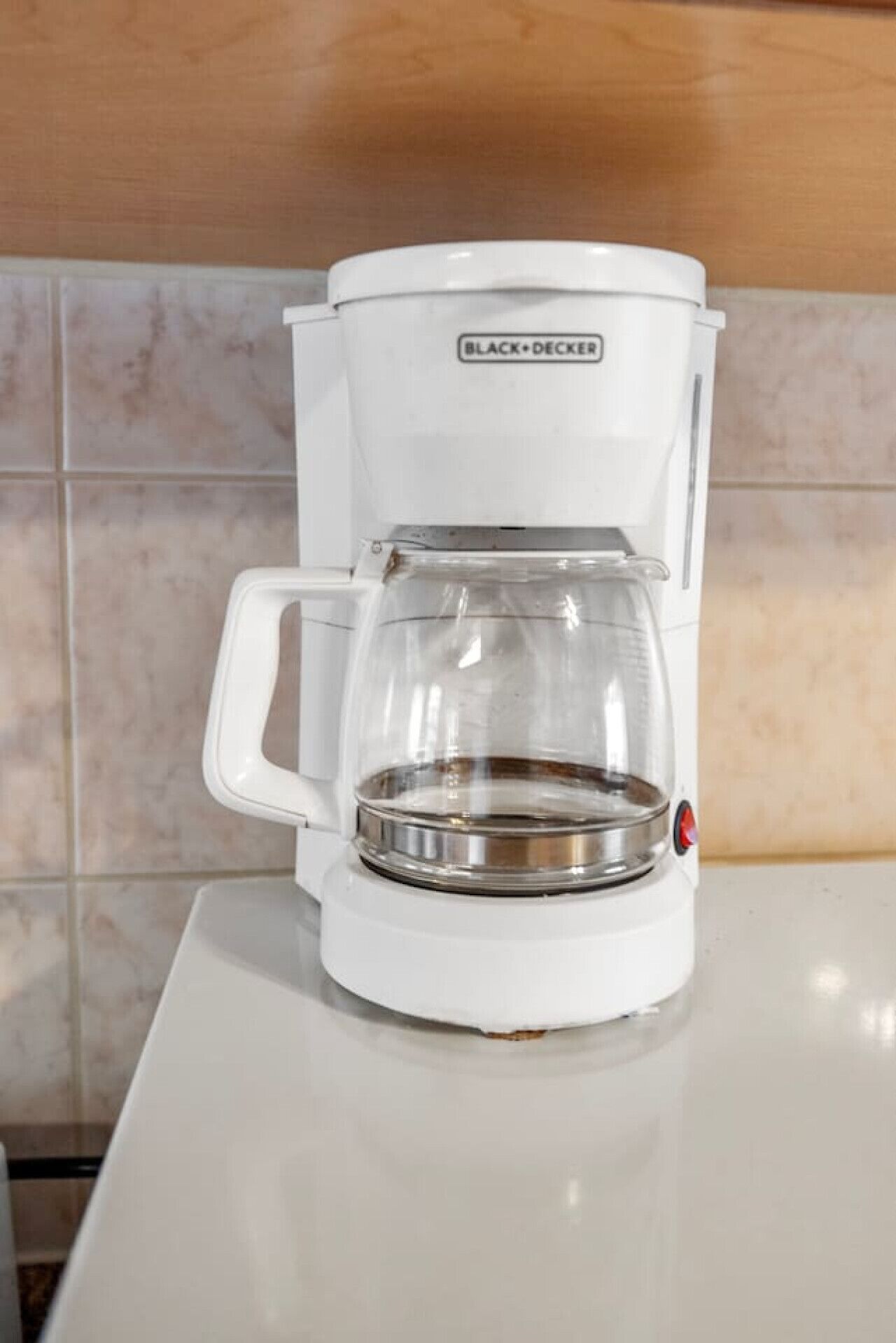 A white coffee maker with a glass carafe on a white countertop.