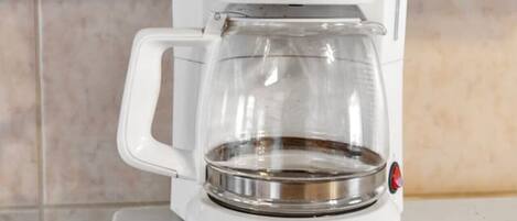 A white coffee maker with a glass carafe on a white countertop.