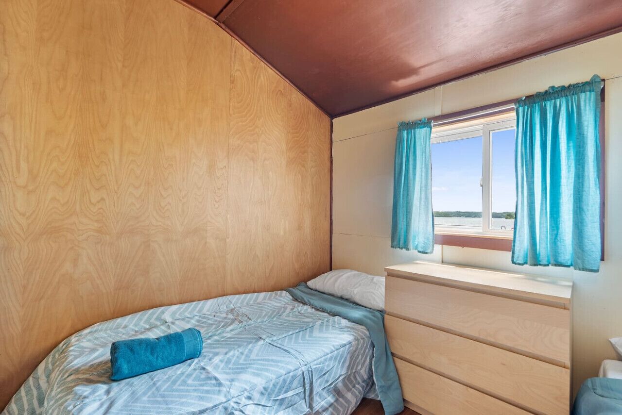 A compact bedroom with a bed, a dresser, and a window with curtains.