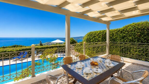 A covered outdoor area with a table set for dining, a pool, and a view of the sea.