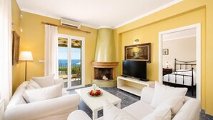 A room with a fireplace, a television, white sofas, and a view of the sea.