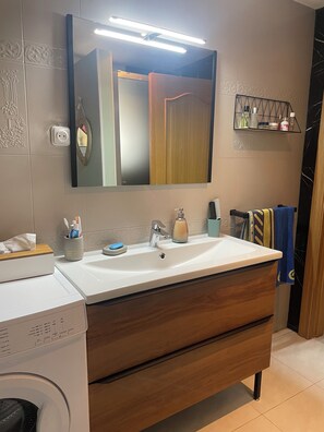 Bathroom features a large mirror, sink, washing machine, and towel rack.