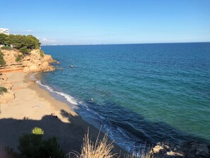 Ein Küstenstrand mit klarem, blauem Wasser, sandigem Ufer und felsigen Klippen.