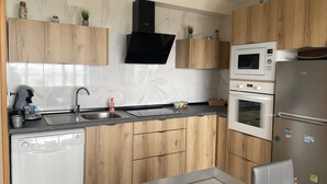 Eine moderne Küche mit Holzausstattung, einer schwarzen Dunstabzugshaube, einer eingebauten Mikrowelle, einem Edelstahlkühlschrank und einem Geschirrspüler.