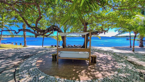 A wooden bed under a tree with a view of a beach and water. - Eden do Catu - BRAGA um paraiso privado a Beira da Lagoa  (Tapera)