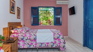 A bedroom with a bed, a nightstand, a lamp, a window with shutters, a TV, and a blue door. - Eden do Catu - BRAGA um paraiso privado a Beira da Lagoa  (Tapera)