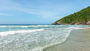 Egy tiszta, sekély vizű strand, homokos parttal és a háttérben egy zöld lejtővel.
