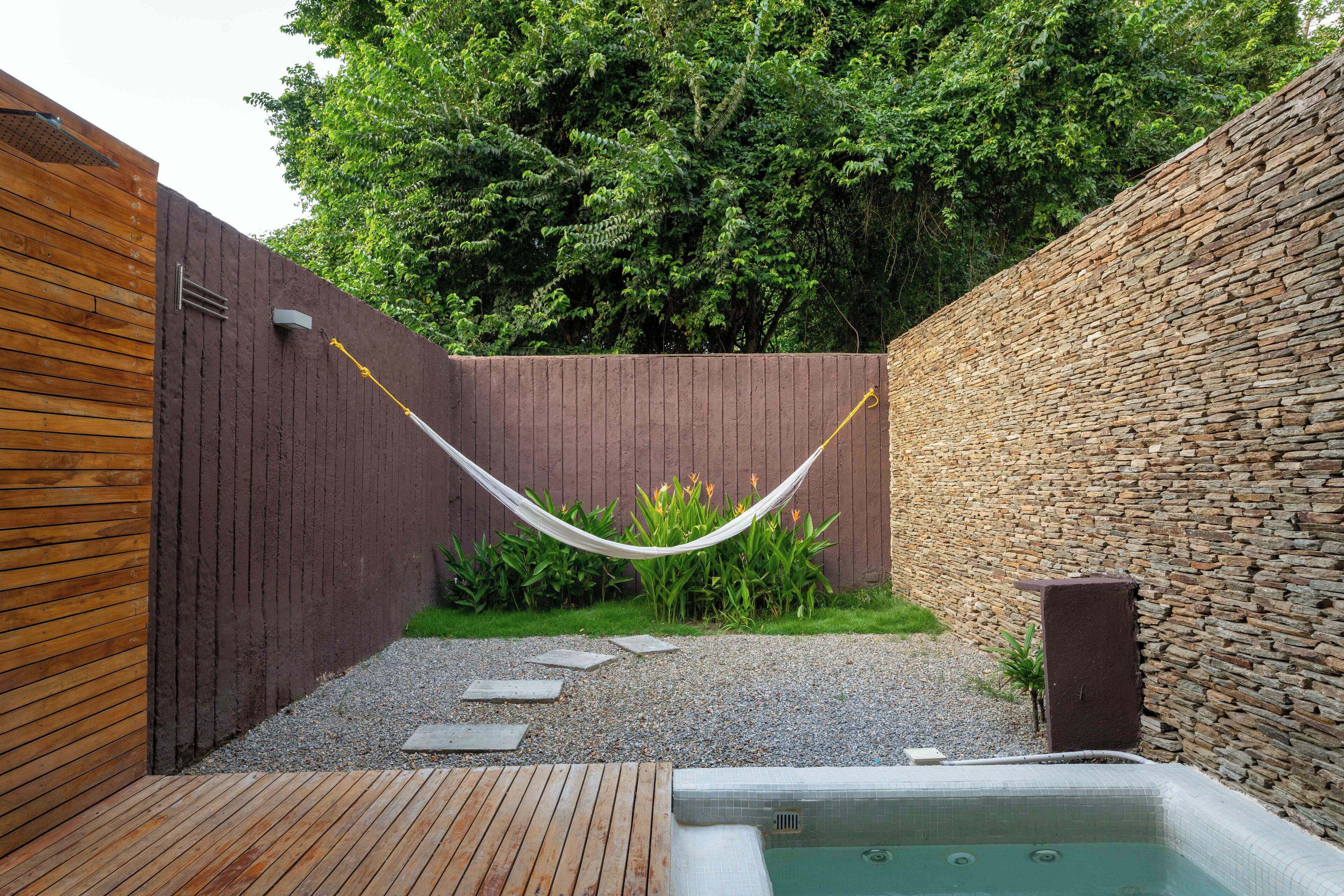 Une terrasse en bois, un mur de pierres, un hamac, un petit jardin et un jacuzzi.