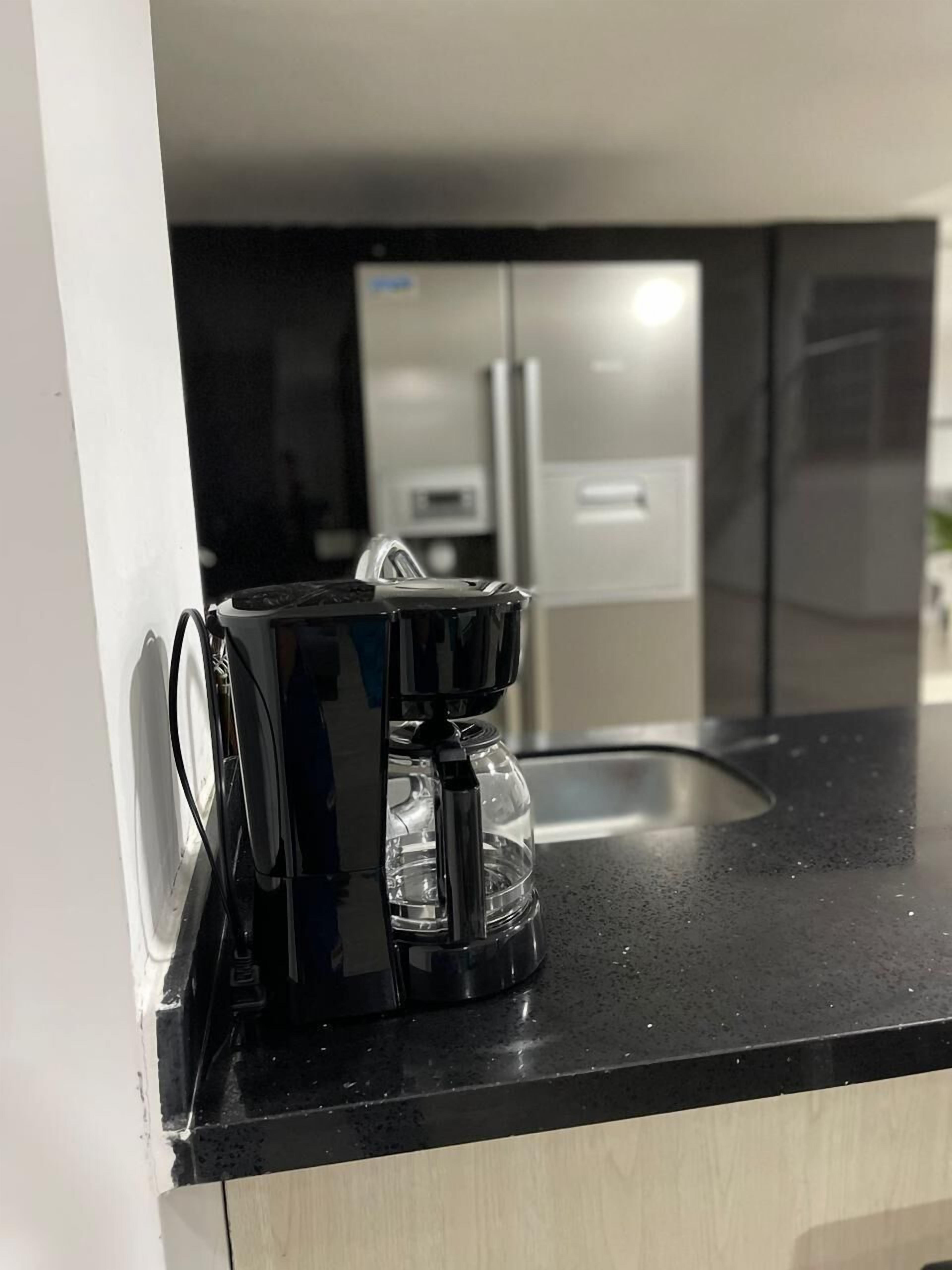 Una cocina con una cafetera en la encimera, un refrigerador al fondo y un lavabo.