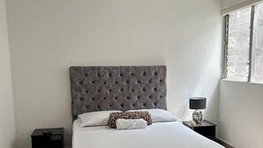 A modern bedroom with a tufted headboard, a large bed, two bedside tables, and a window with a view. - CASA LAURELES ESTADIO MEDELLIN (Medellín)