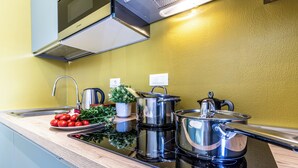 A modern kitchen with a black induction cooktop, stainless steel pots, a kettle, and a potted plant. - HouSmart Emilia Levante 98 (Bologna)