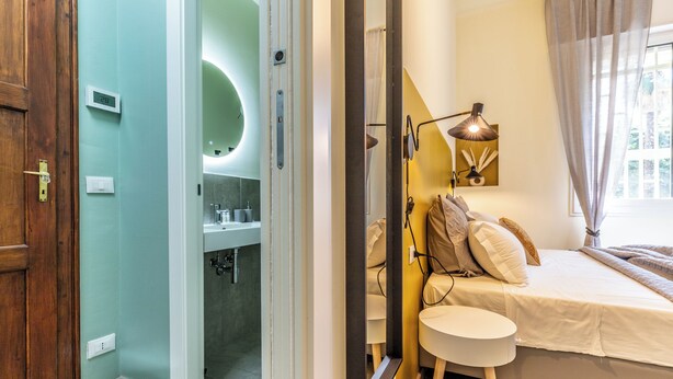 A bedroom with a bed, bedside table, and a mirror. - HouSmart Emilia Levante 98 (Bologna)