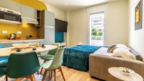 A compact living space with a kitchenette, a dining area, a sofa, and a window with a view of the outside. - HouSmart Emilia Levante 98 (Bologna)