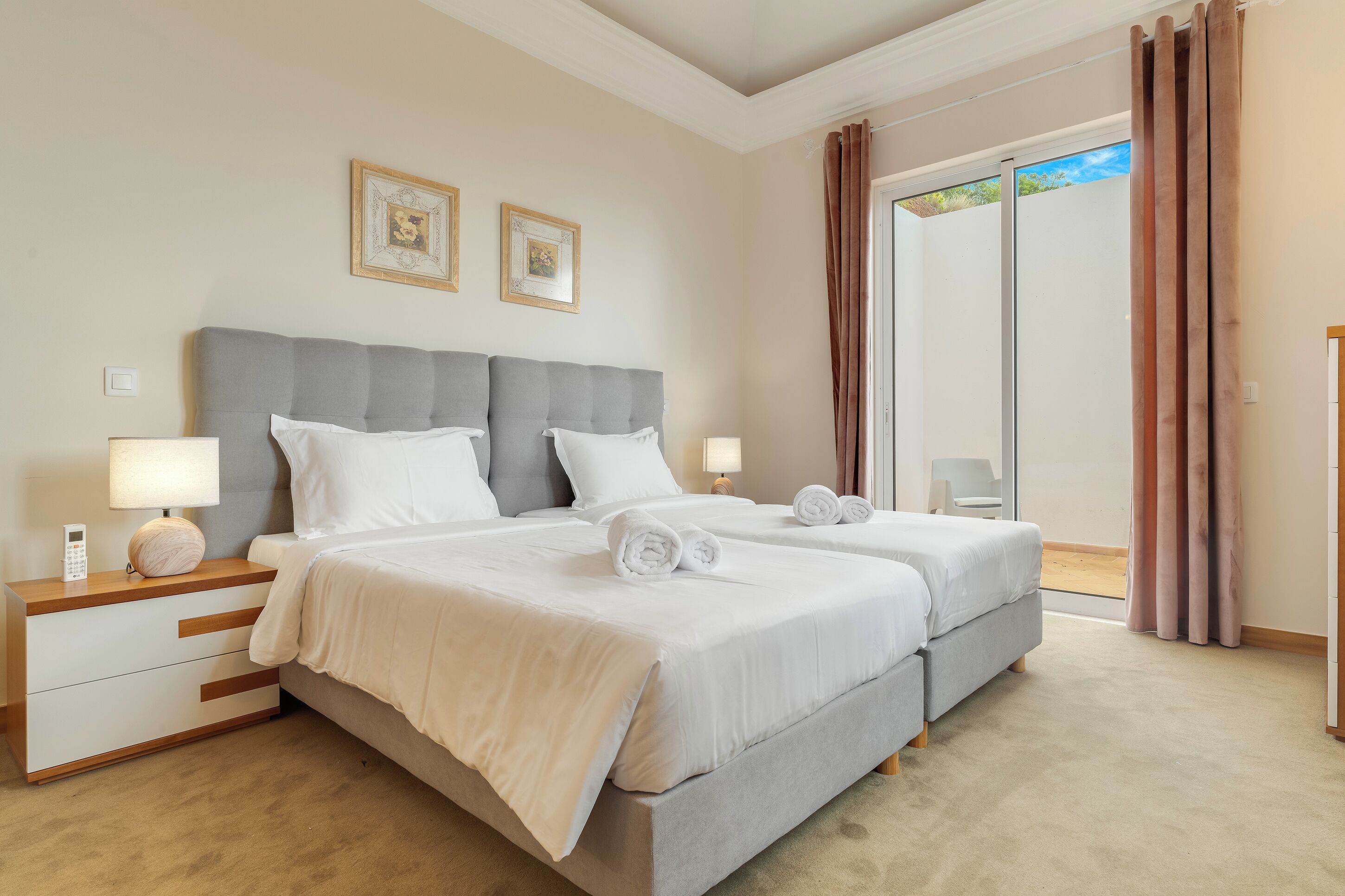 A double bed with a grey headboard, two bedside tables with lamps, and two framed pictures on the wall.