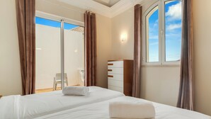 Habitación de hotel con dos camas, un armario, una silla y vista al cielo a través de una ventana.