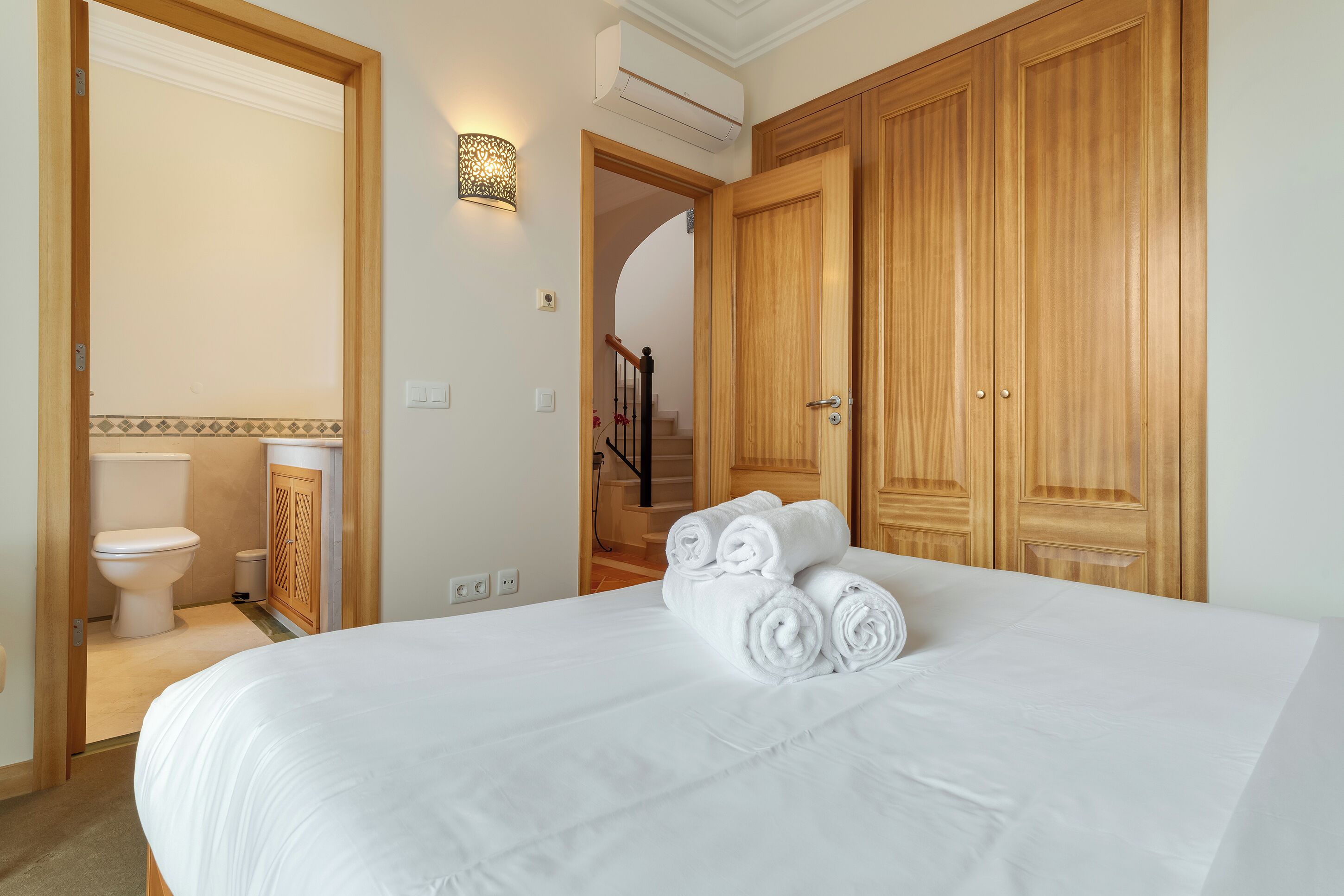 A hotel room with a large bed, wooden wardrobe, a bathroom with a toilet, and a staircase leading to another floor.