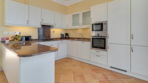 Una cocina con gabinetes blancos, encimera de granito, microondas, horno y lavaplatos.