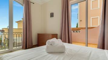A hotel room with a bed, a wooden dresser, and a balcony with curtains.
