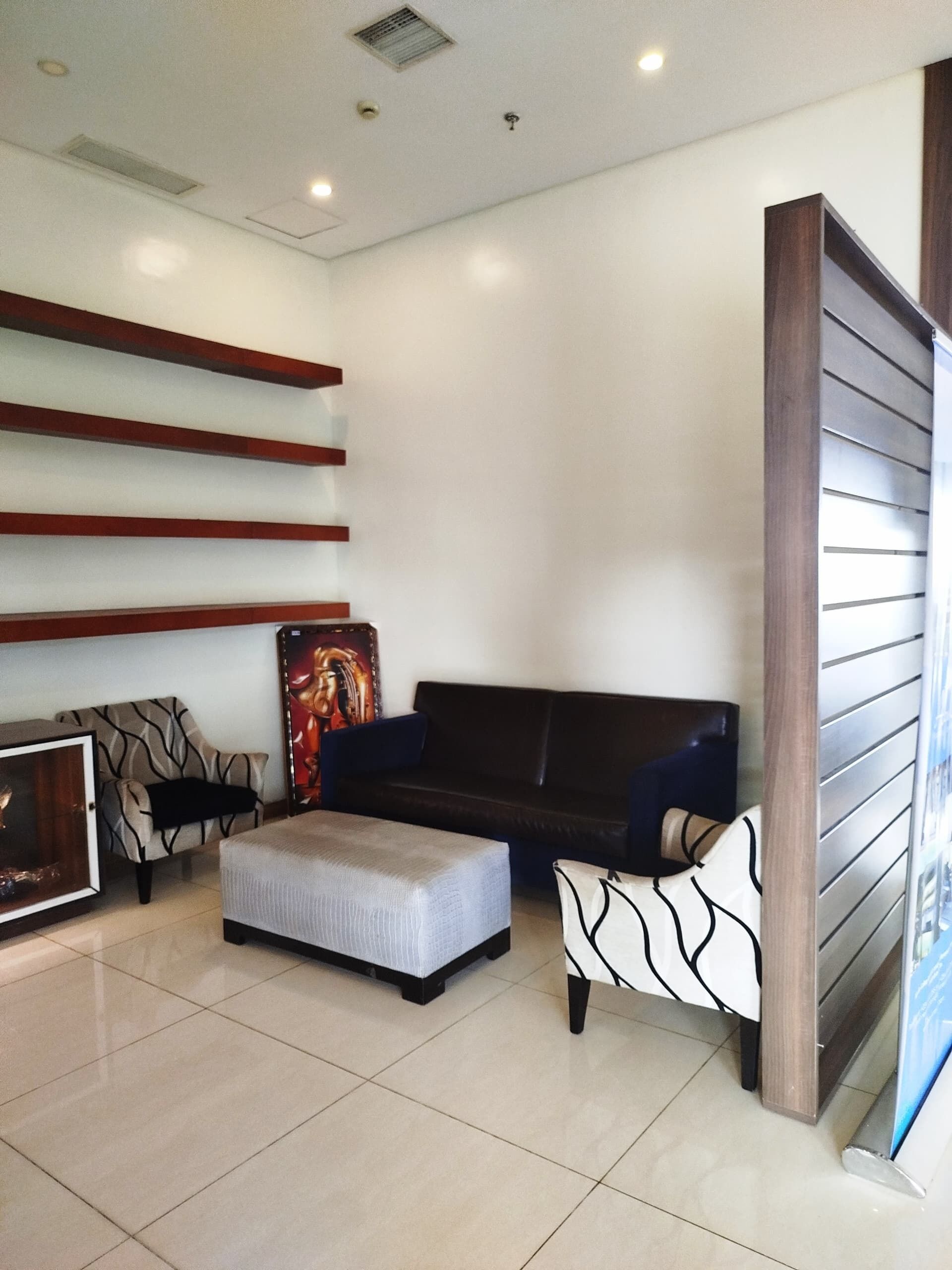 A modern living room with a dark sofa, a patterned armchair, and a white ottoman.