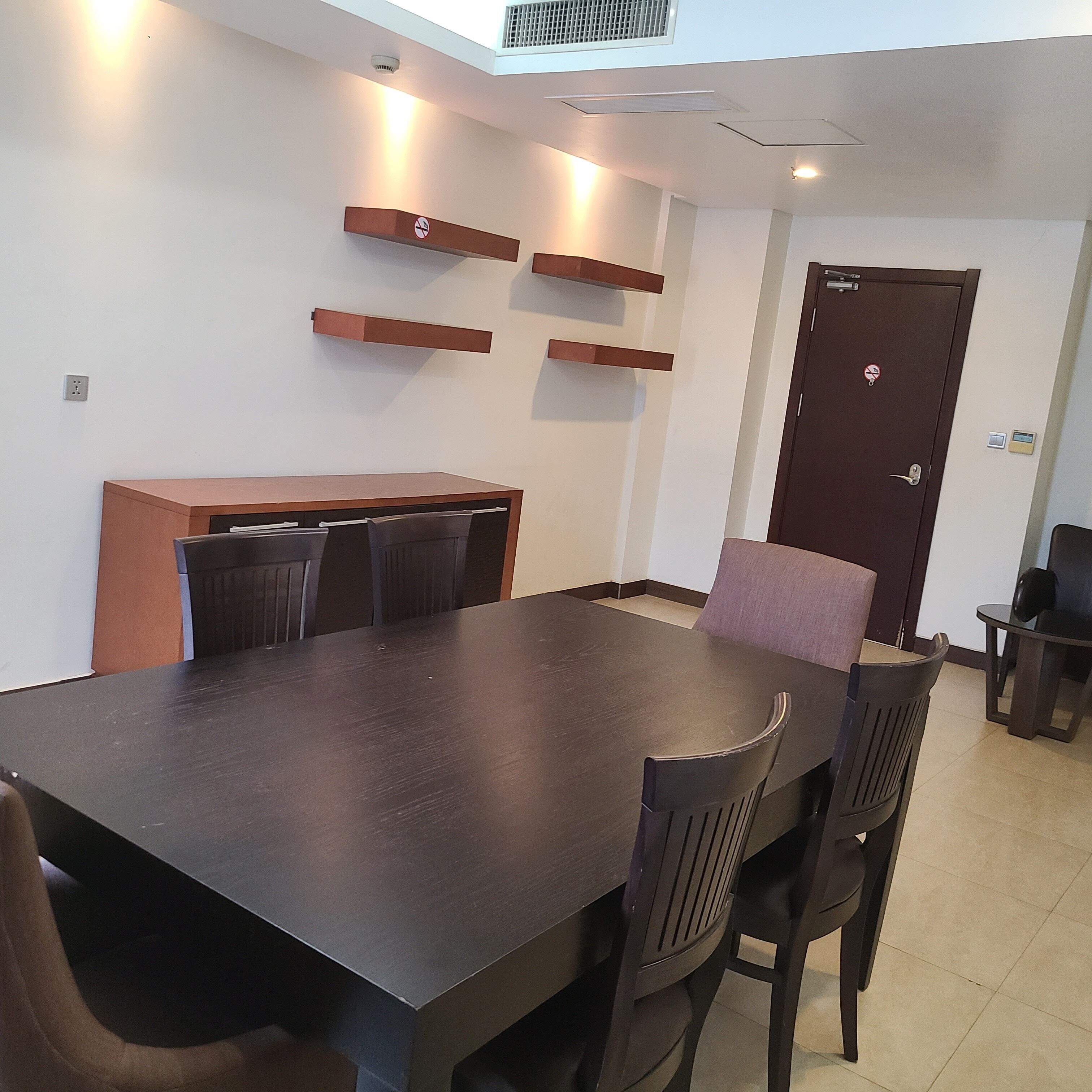 Una sala de conferencias con una mesa de madera oscura, cuatro sillas y una puerta marrón con cerradura.