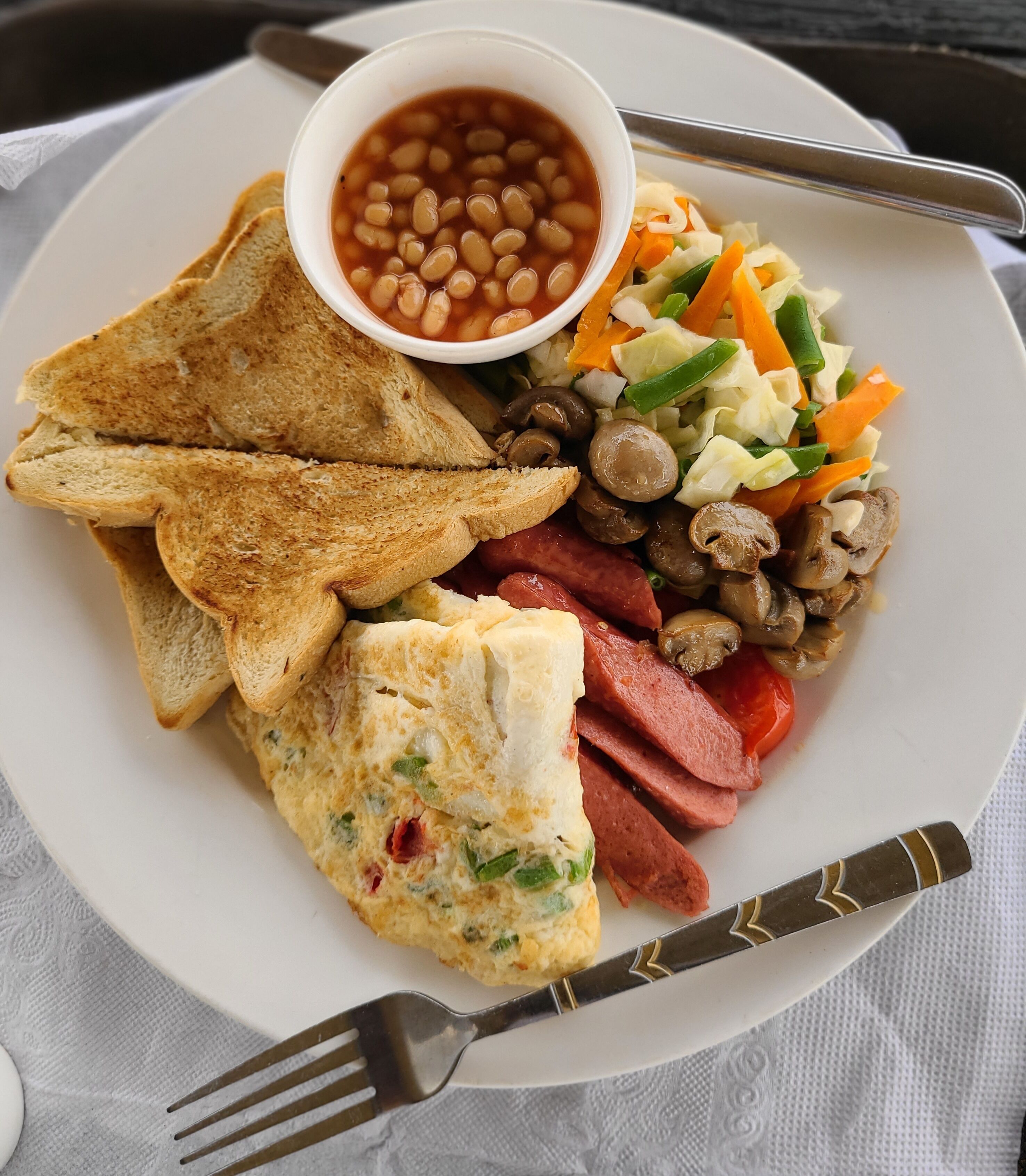 A plate with toast, beans, a salad, sausages, and an omelette.