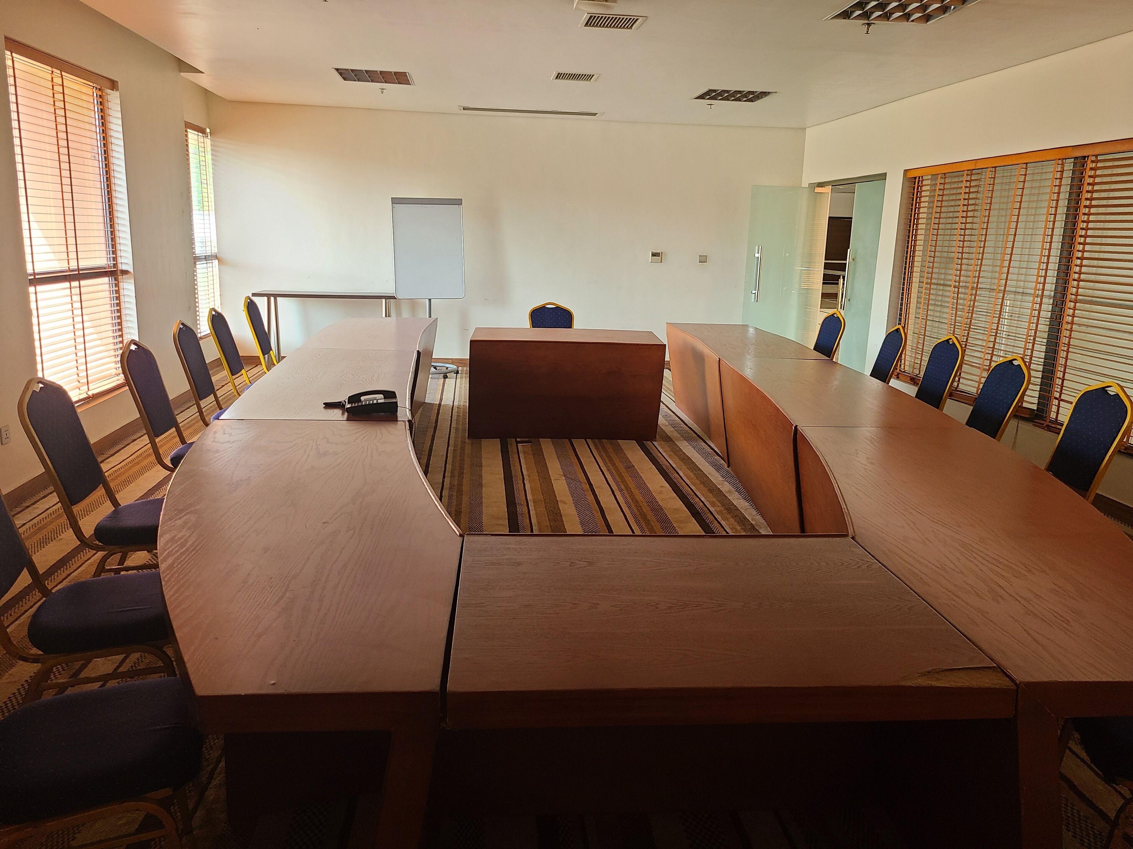 A conference room with a long wooden table, blue cushioned chairs, a whiteboard, and a carpeted floor.