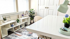 A bright room with a white desk, shelves with plants, and a door with a checkered pattern.