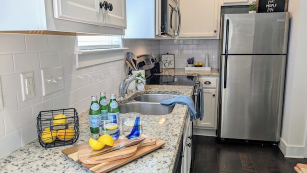 A kitchen with white cabinets, a stainless steel refrigerator, a granite countertop, and a black wire basket with lemons.