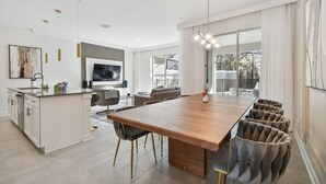 Una cocina moderna con una isla de madera, armarios blancos y un amplio comedor con sillas tapizadas.