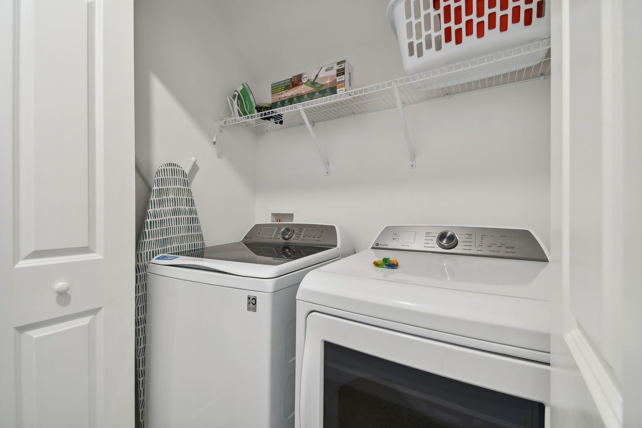 Ett tvättrum med tvättmaskin, torktumlare och en hylla med tvättkorgar.
