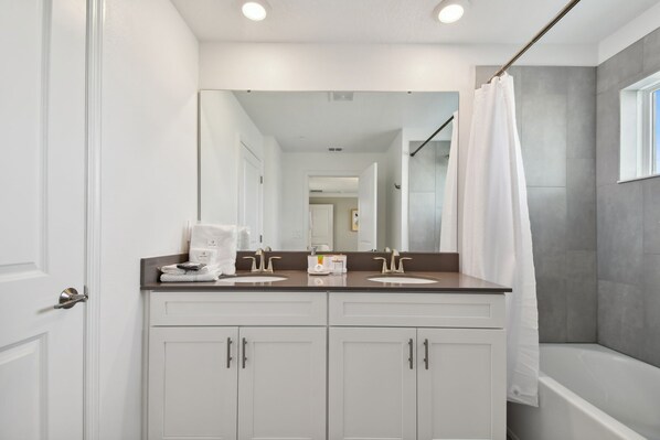 A bathroom with a double sink vanity, a shower with a curtain, and a large mirror above the sink.
