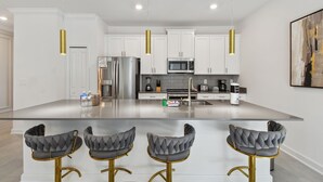 Una cocina moderna con armarios blancos, electrodomésticos de acero inoxidable y una isla central con taburetes de bar.