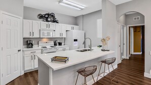 Eine moderne Küche mit weißen Schränken, einer zentralen Kochinsel mit Hockern und einer eingebauten Mikrowelle.