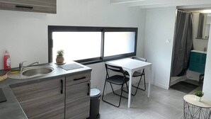A compact kitchen with a window, a sink, a small table, and a chair. - Cosy downtown studio - ideal location (Challans)