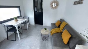 A modern living space with a dining table, chairs, a sofa with cushions, a small round table with a plant, and a mirror on the wall. - Cosy downtown studio - ideal location (Challans)