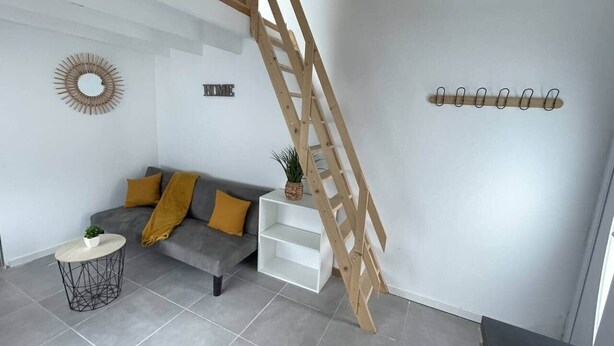 A modern living room with a grey sofa, a small round table, a white storage unit, and a wooden ladder against the wall. - Cosy downtown studio - ideal location (Challans)